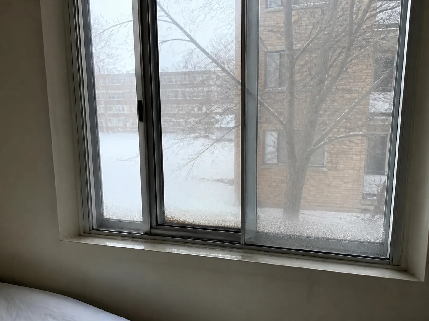 Old silver aluminum slider window with condensation and frost along the bottom of the glass in winter