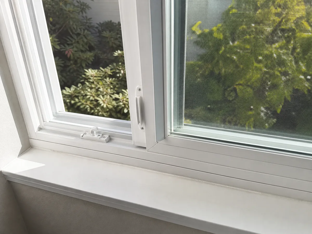 Close-up of a new white vinyl slider window partly open, showing the track, meeting rail, lock and screen