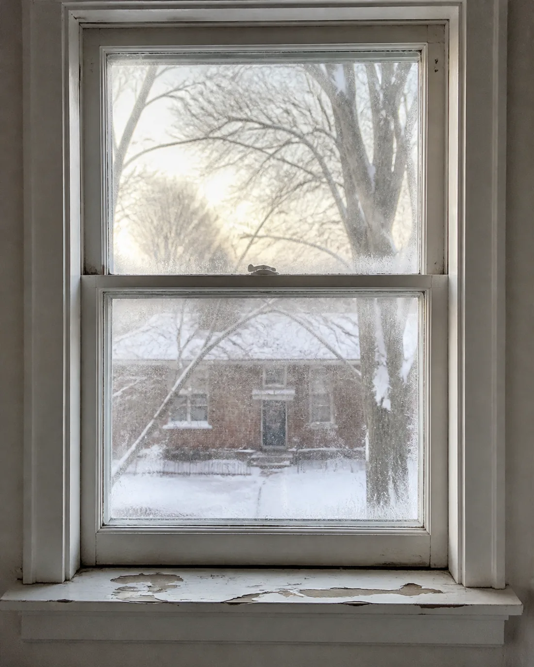 Old single-pane wood double-hung window with peeling paint and frost on the glass in winter