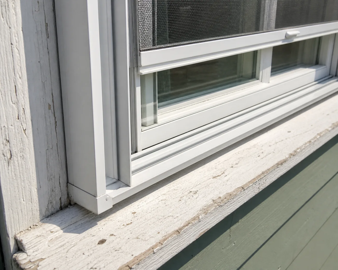 Close-up of a white aluminum triple-track storm window over an old painted wood window, screen half raised